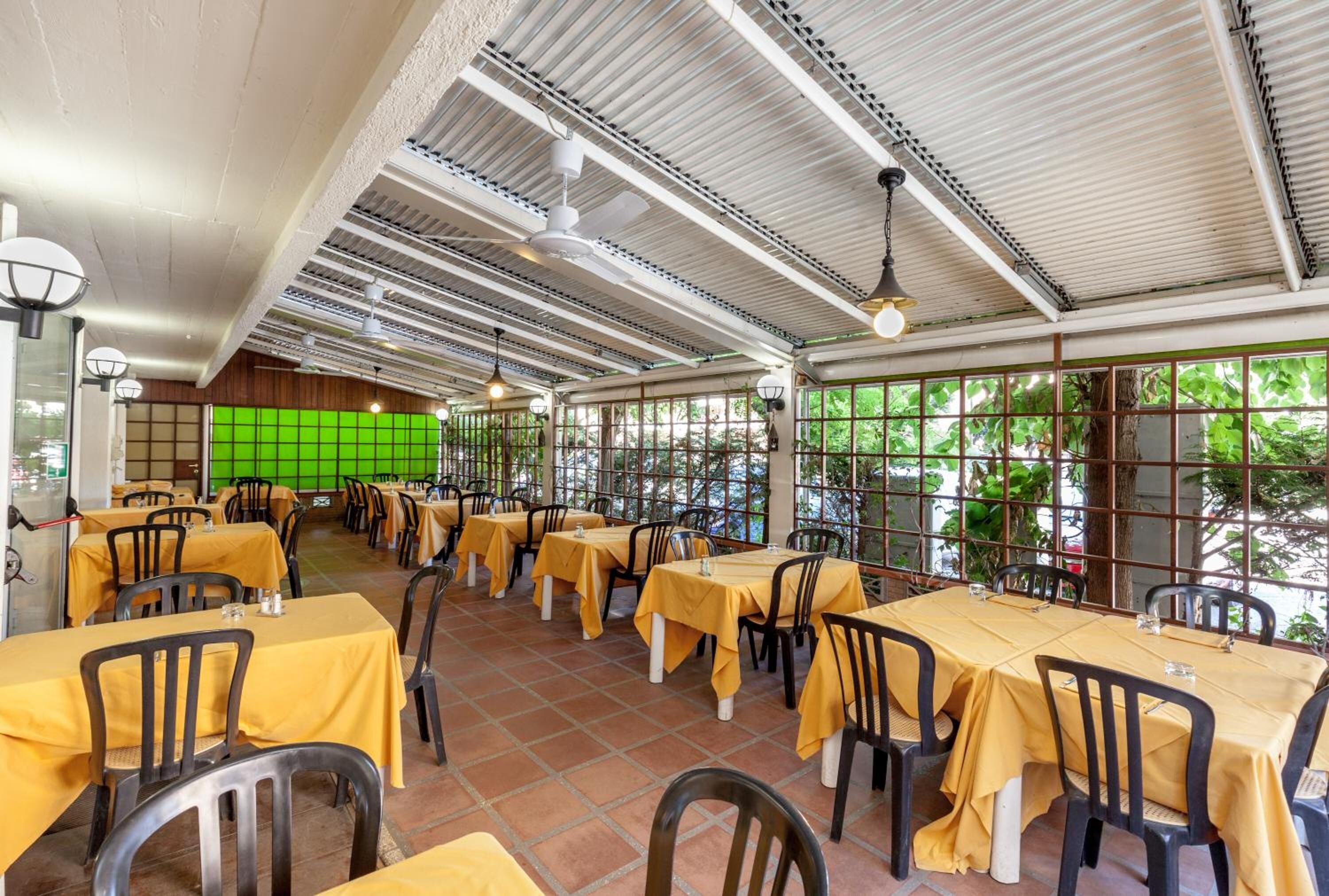 Ein Restaurant mit gelben Tischdecken, schwarzen Stühlen und einer grünen Trennwand.