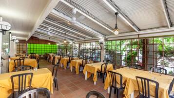 Ein Restaurant mit gelben Tischdecken, schwarzen Stühlen und einer grünen Trennwand.