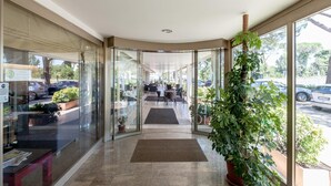 A hotel lobby with glass doors, a reception desk, and a potted plant. - Hotel Tevere (Perugia)