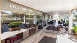 A reception area with a bar and restaurant sign, outdoor seating with wicker furniture, and potted plants. - Hotel Tevere (Perugia)