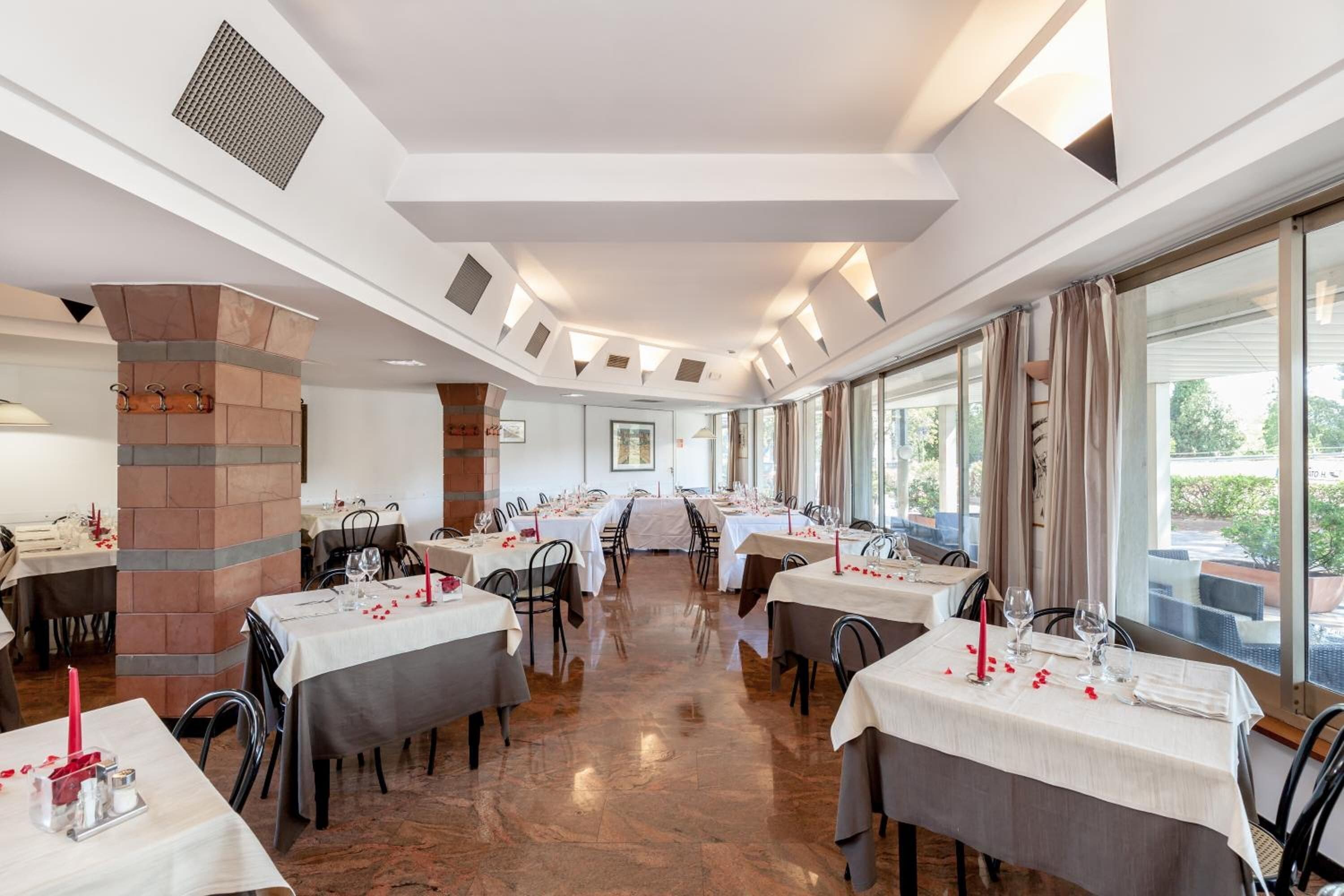 Un restaurante con mesas dispuestas para comer, un pilar de ladrillo y ventanas grandes.