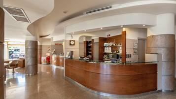 Un lobby moderno de hotel con un mostrador de recepción curvo, zona de estar y un reloj en la pared.