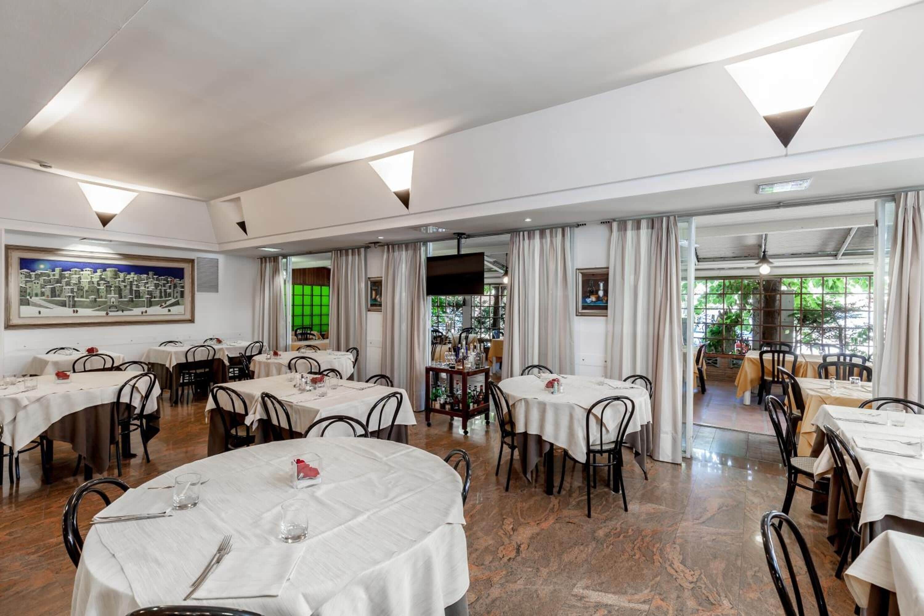 Un espace repas avec des tables rondes, des chaises et un grand tableau accroché au mur.