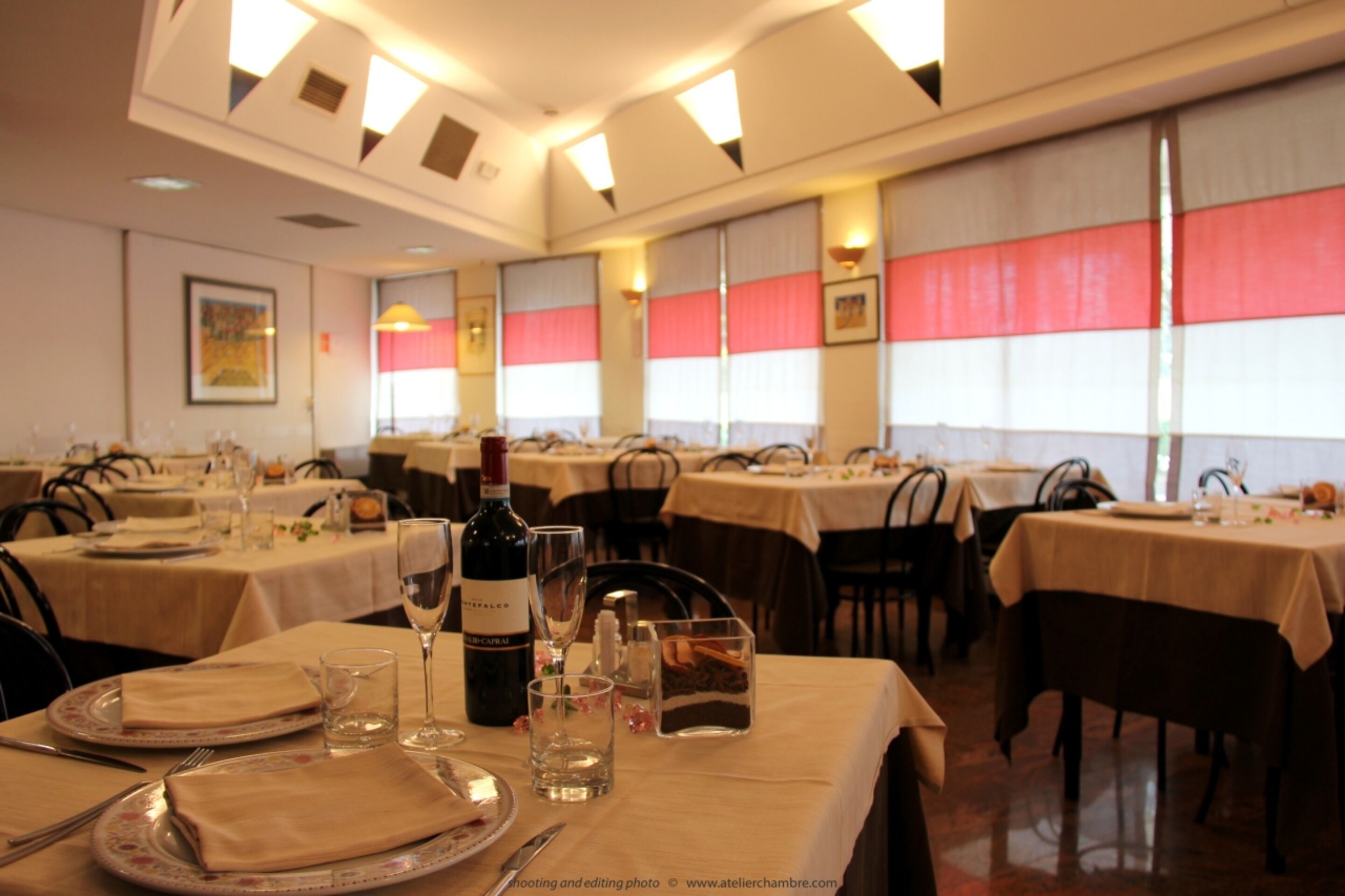 A dining area with multiple tables set for a meal, featuring a bottle of wine, glasses, and neatly arranged cutlery.