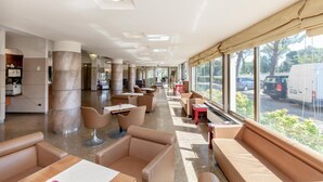 A spacious hotel lobby with leather seating, large windows, and a view of the parking area. - Hotel Tevere (Perugia)