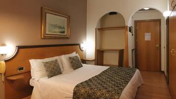 Una camera d'albergo con un letto, un telefono sul comodino, un quadro appeso al muro e una porta con un cartello.