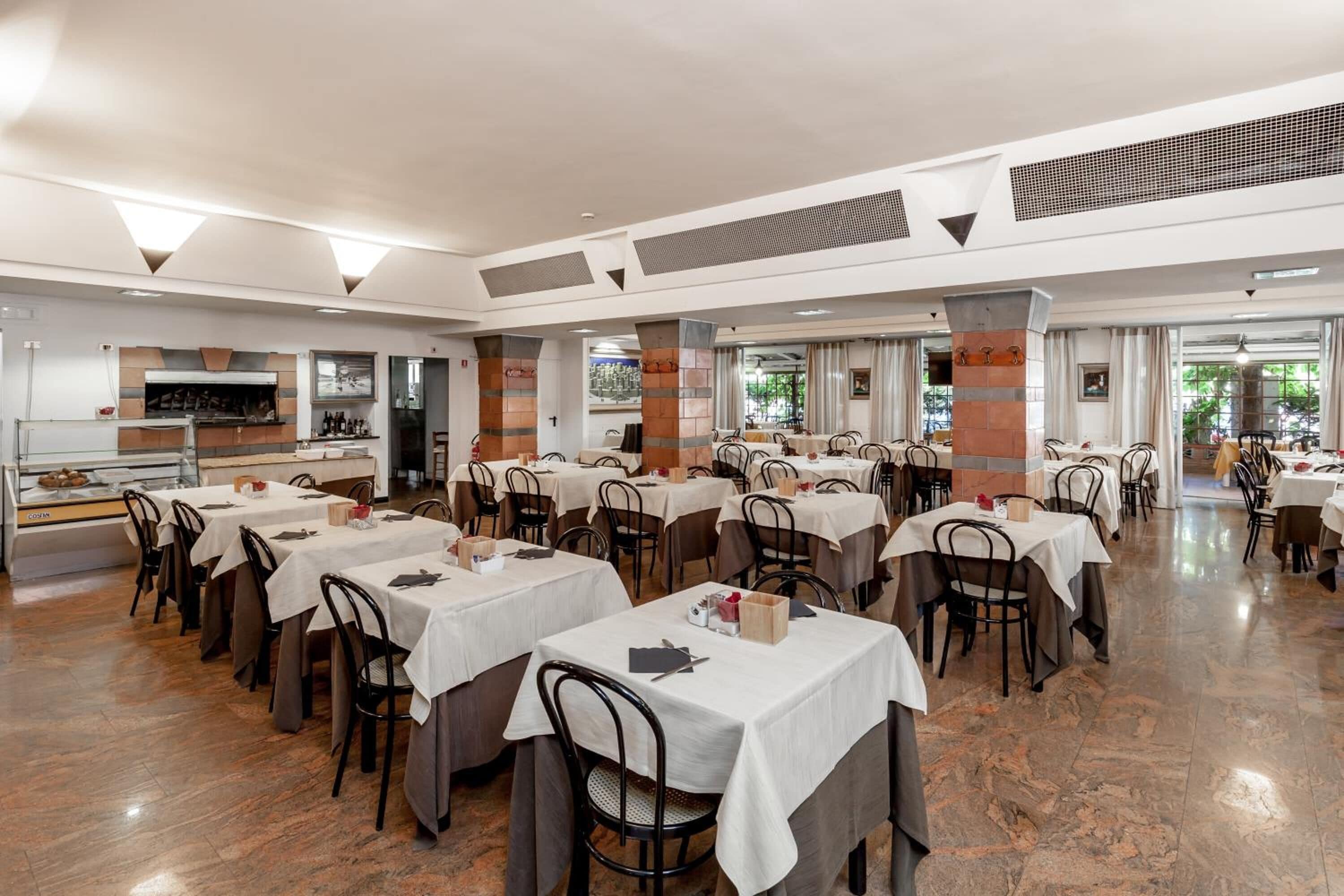 A spacious restaurant with multiple tables and chairs, a counter with a display case, and a large window providing a view of the outdoors.