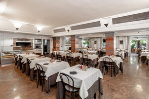 Un restaurante amplio con varias mesas y sillas, una barra con vitrina y un ventanal con vistas al exterior.