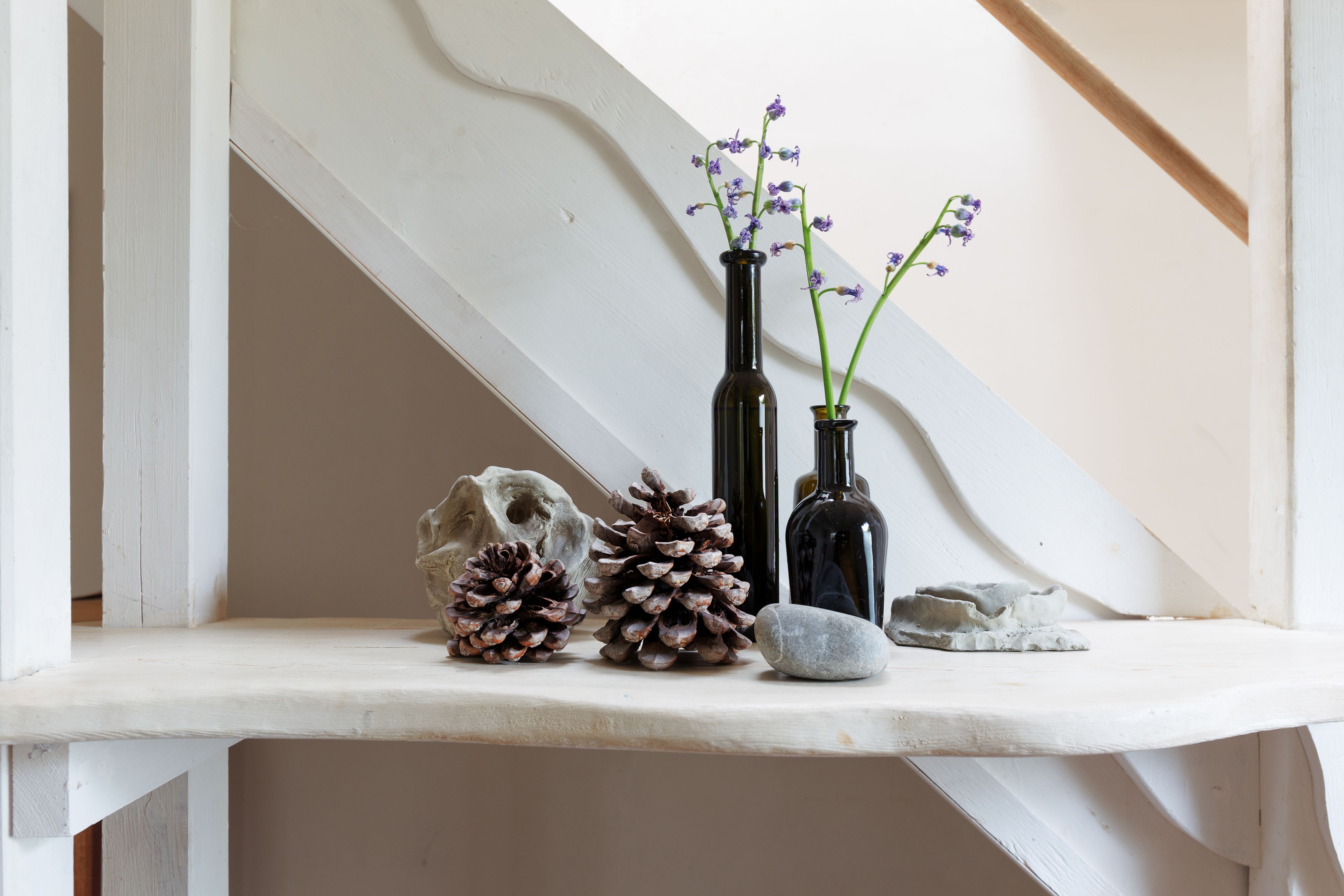 Una estantería con elementos decorativos, incluyendo piñas, un cráneo y dos jarrones con flores.