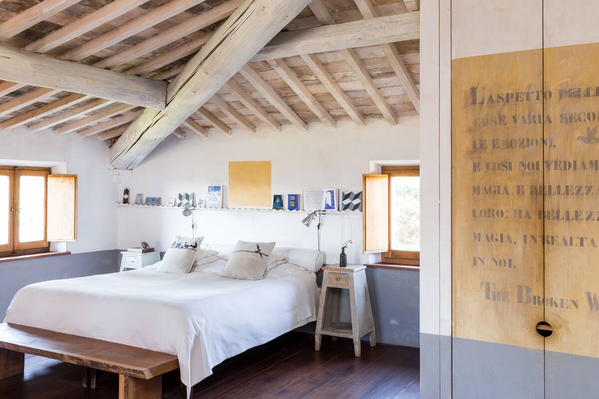 Une chambre avec un plafond en bois, un grand lit, des tables de chevet et un mur orné de texte.