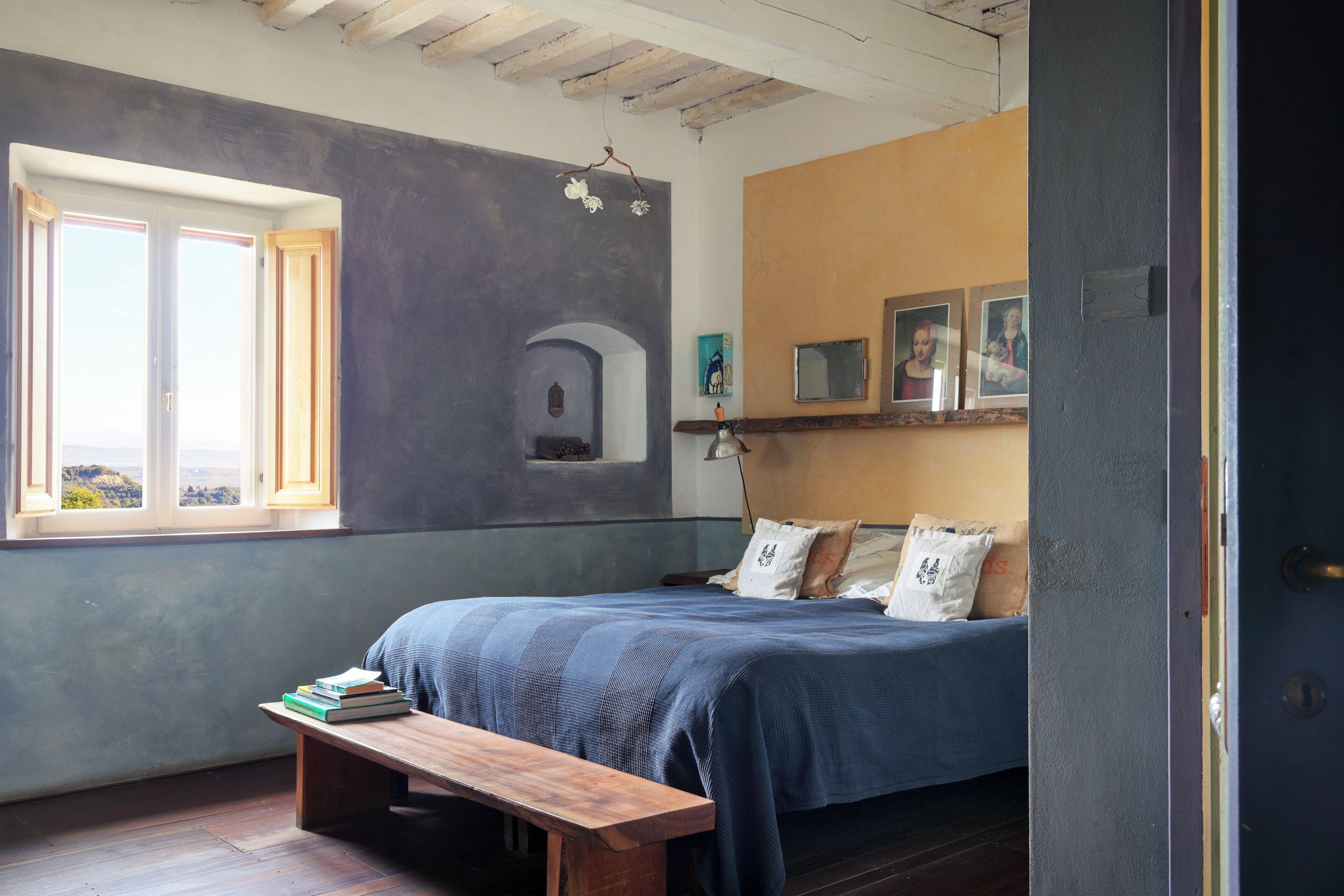 Una camera da letto con un letto, una panca, una finestra e uno scaffale con fotografie.