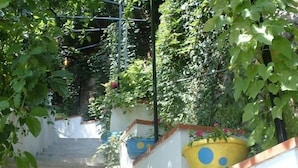 A narrow staircase with steps leading upwards, surrounded by lush greenery and potted plants. - Giardino dei Limoni (Ravello)