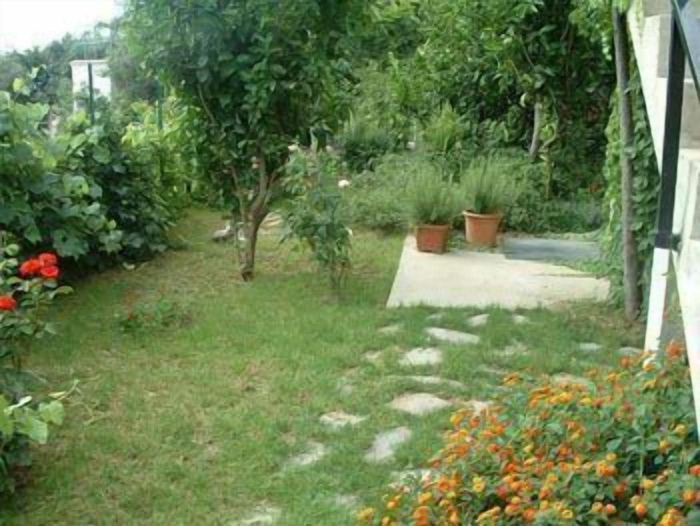 Un jardín con sendero pavimentado, plantas en macetas y plantas con flores.