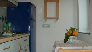 A kitchen with a blue refrigerator, a table with a floral tablecloth, and a vase with oranges and leaves. - Giardino dei Limoni (Ravello)