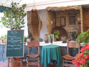 An outdoor dining area with a chalkboard menu, rustic wooden chairs, a table with a green tablecloth, and potted plants. - Campo Golf Bungalows (San Bartolomé de Tirajana)