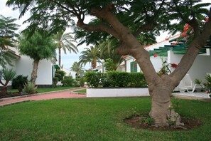 A well-maintained garden with a large tree, a white building with green accents, and a staircase with red flowers.