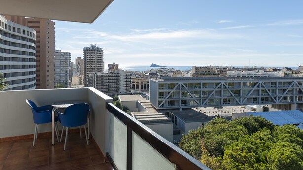 A balcony with a table and chairs, overlooking a cityscape with various buildings and a distant mountain. - Benidorm Apartamentos Michelangelo (Benidorm)