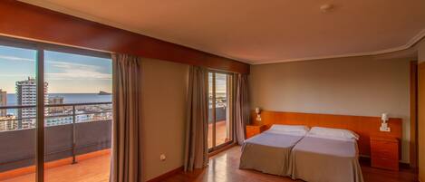 A hotel room with a balcony, a double bed, a nightstand, and a view of the city and sea.