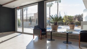 A spacious room with large windows, a seating area with chairs and a table, and a view of a pool and palm trees outside. - Benidorm Apartamentos Michelangelo (Benidorm)
