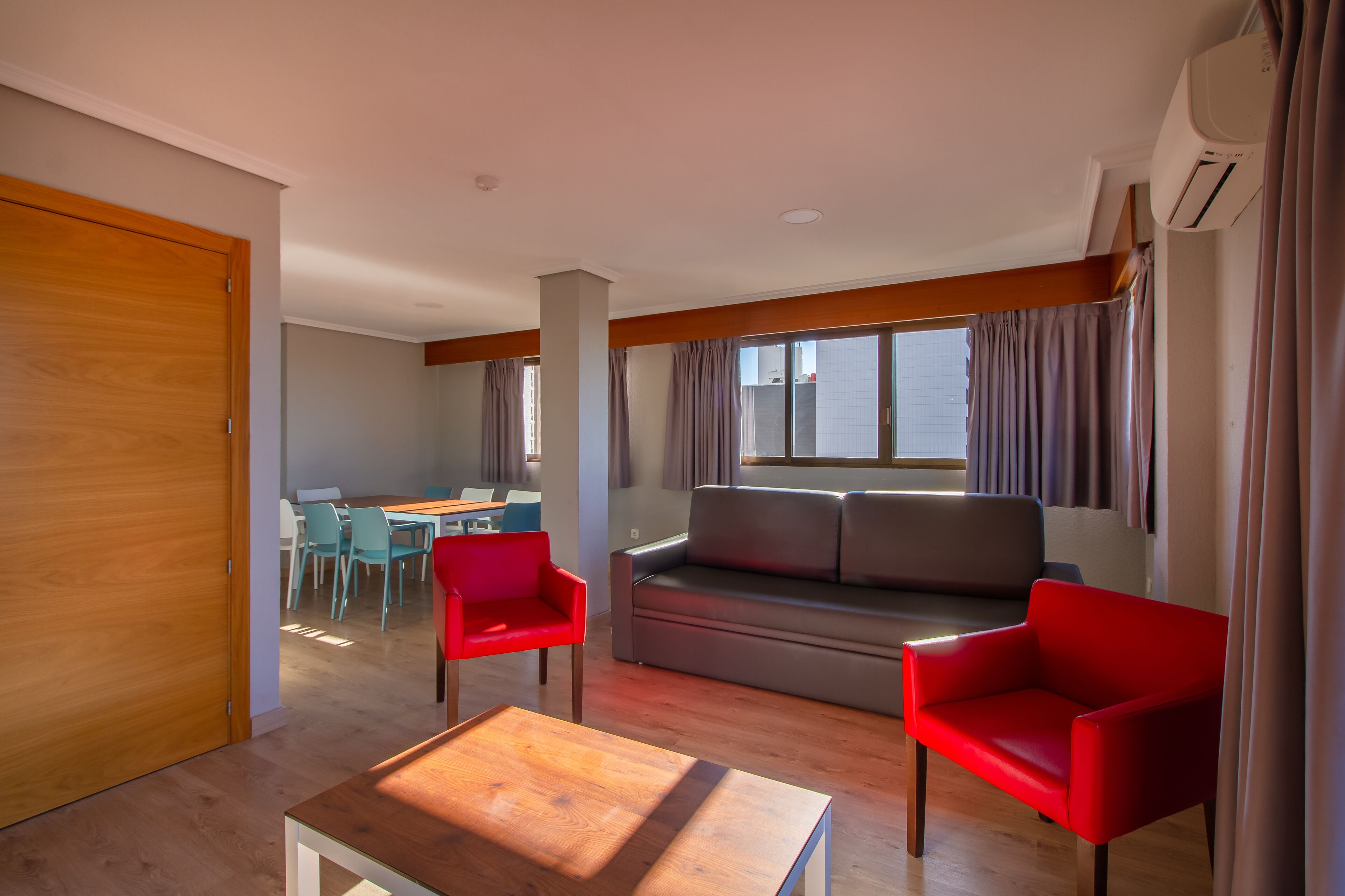 A modern living room with a sofa, two red chairs, a wooden coffee table, and a dining area with a table and chairs.