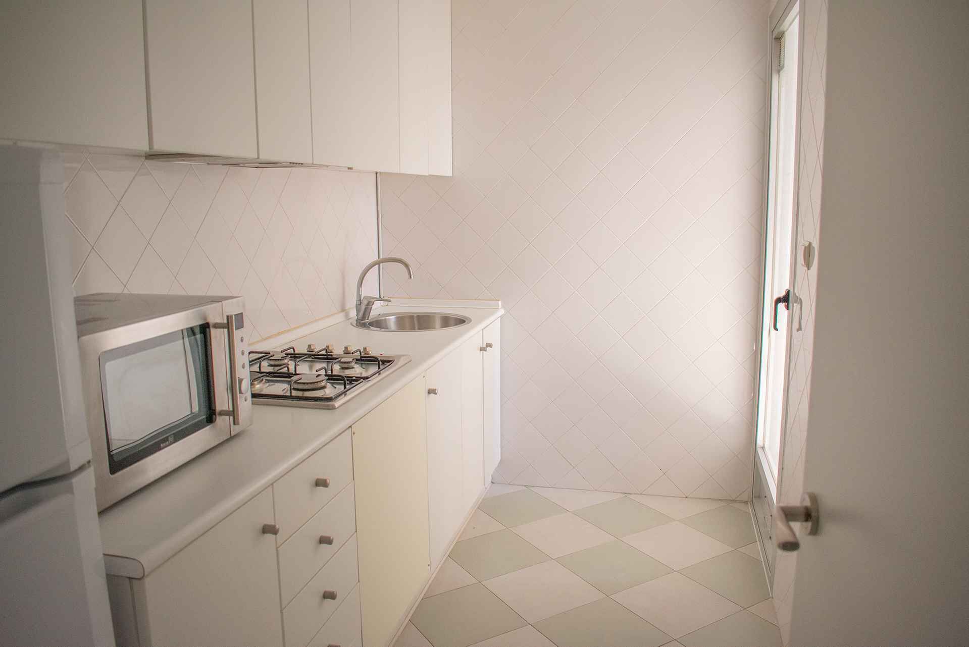 Une petite cuisine avec des meubles blancs, une cuisinière à gaz, un four à micro-ondes et un évier.
