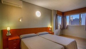 A hotel room with two beds, a round wall light, a window with curtains, and a wooden floor. - Benidorm Apartamentos Michelangelo (Benidorm)