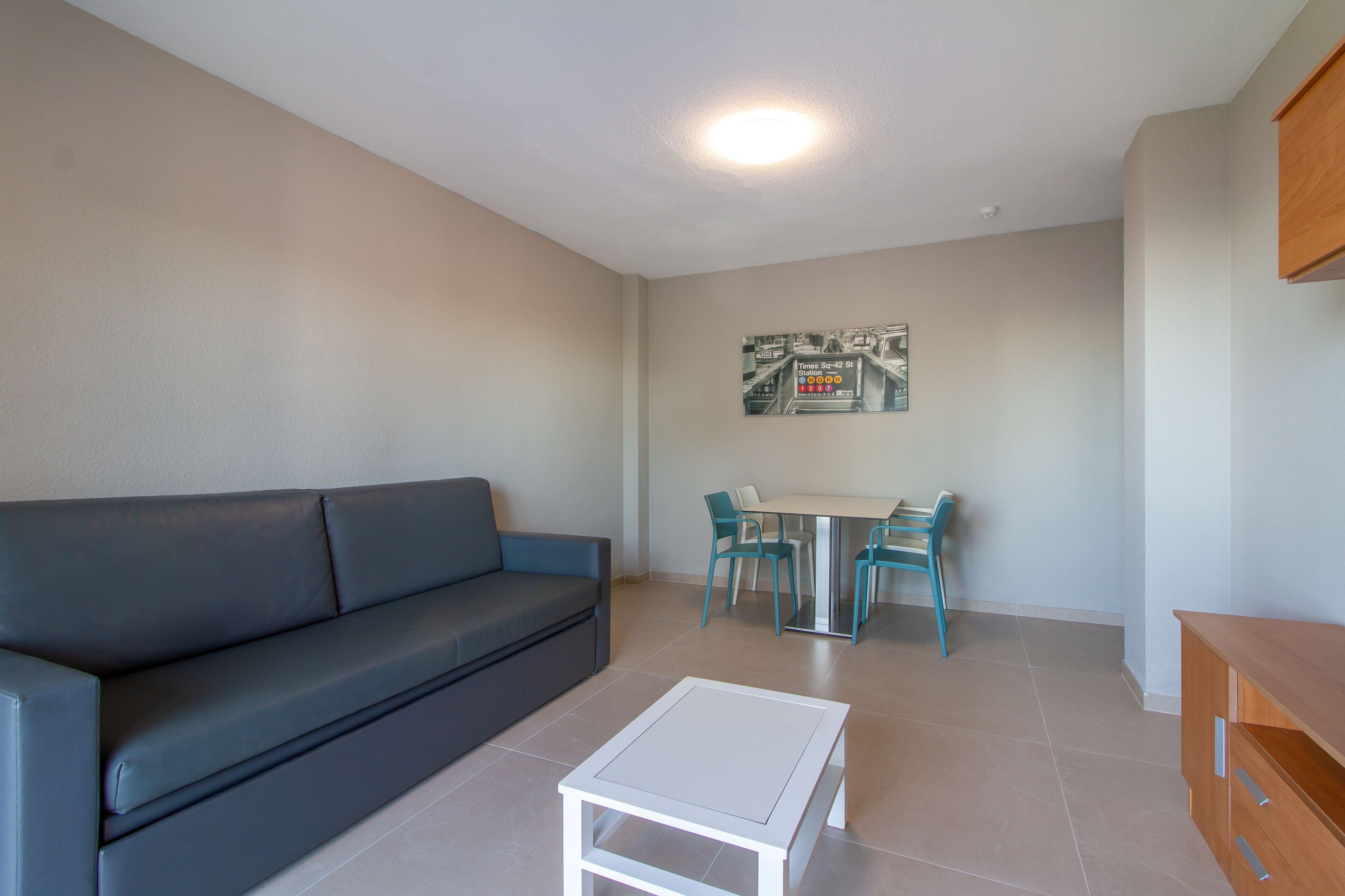 A modern living room with a dark grey sofa, a white coffee table, and a dining area with a glass table and teal chairs.