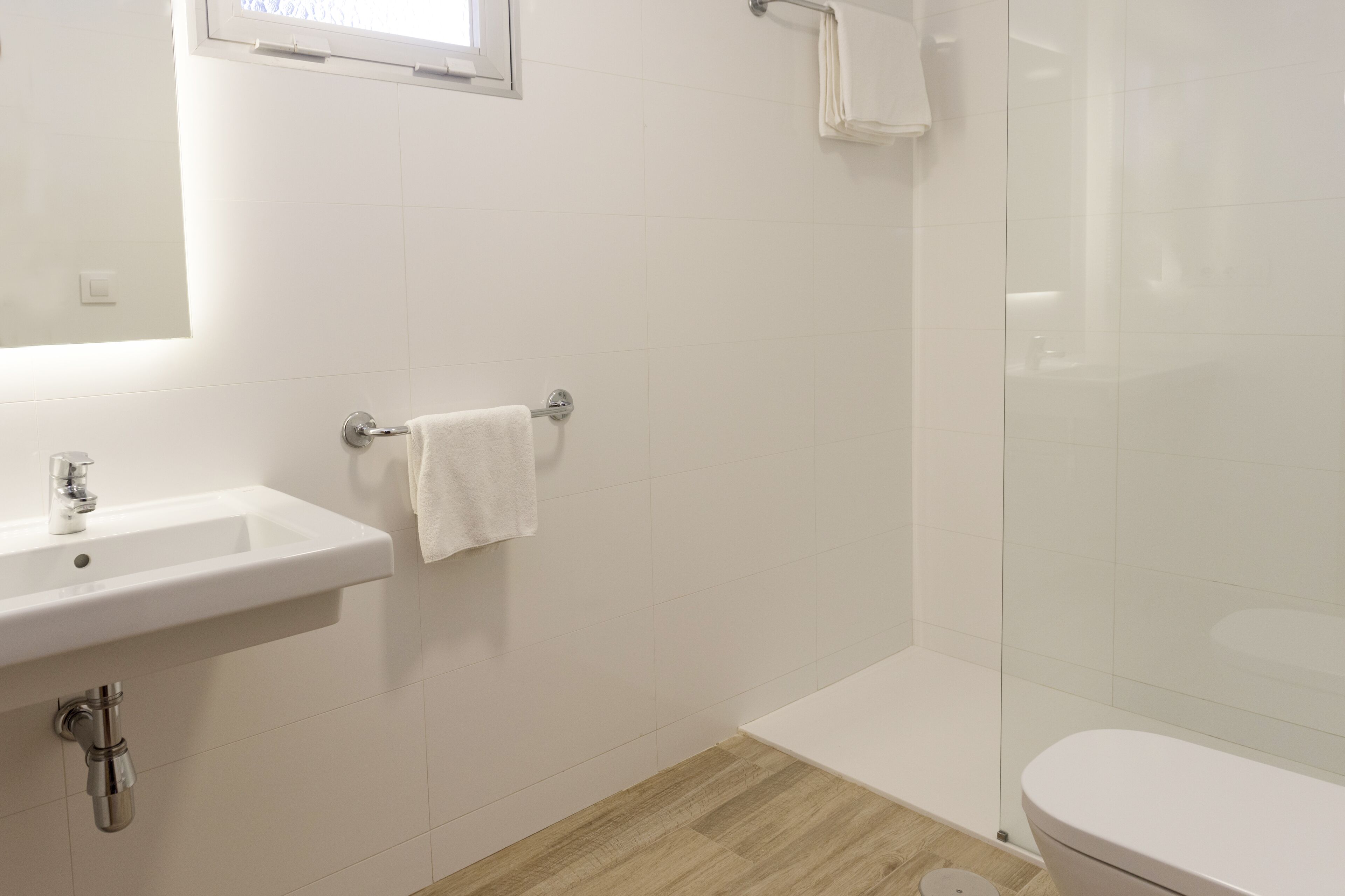Un baño con lavamanos blanco, espejo, toallero, cabina de ducha de vidrio y inodoro.