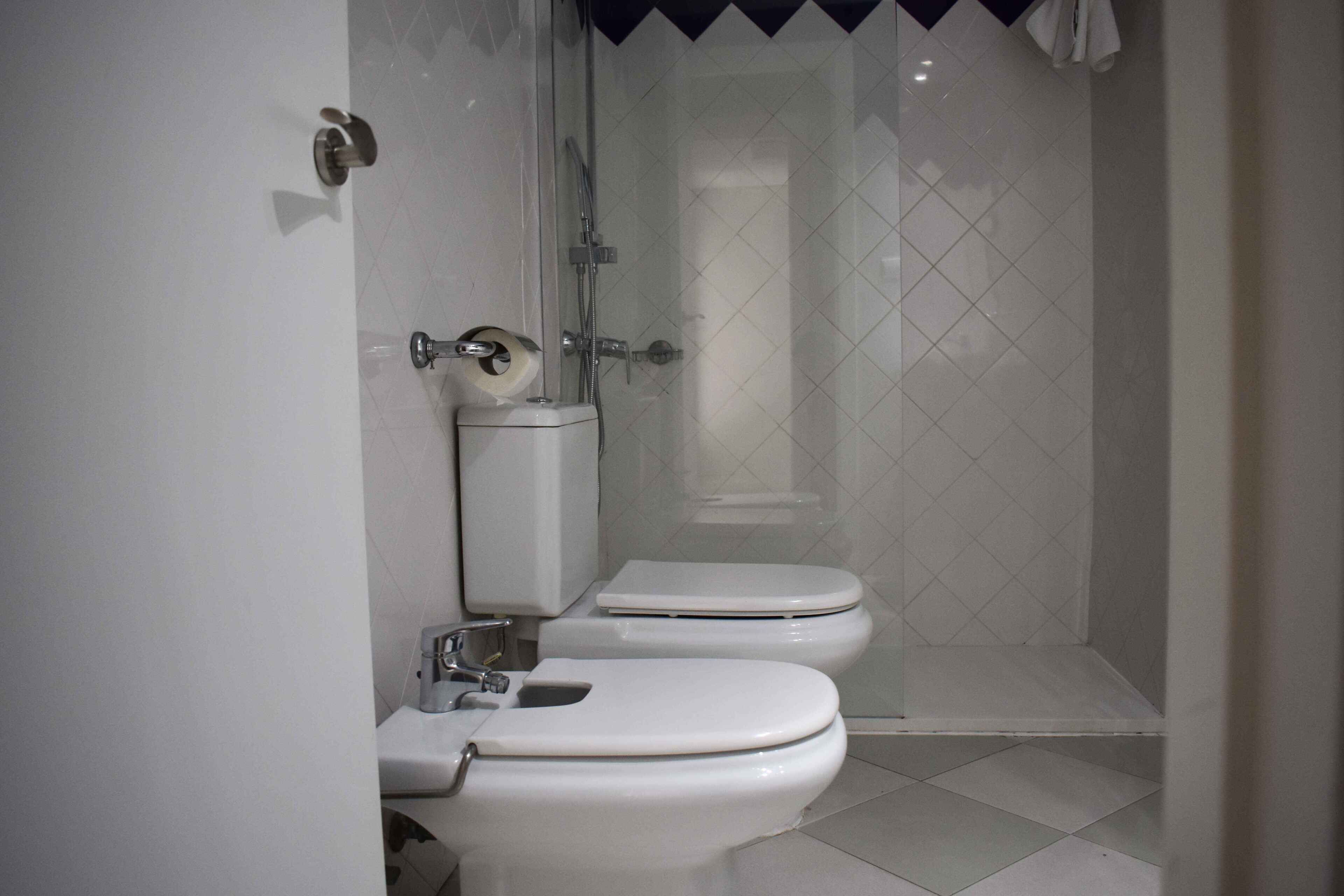 Un baño con dos inodoros, una ducha y un dispensador de papel higiénico.