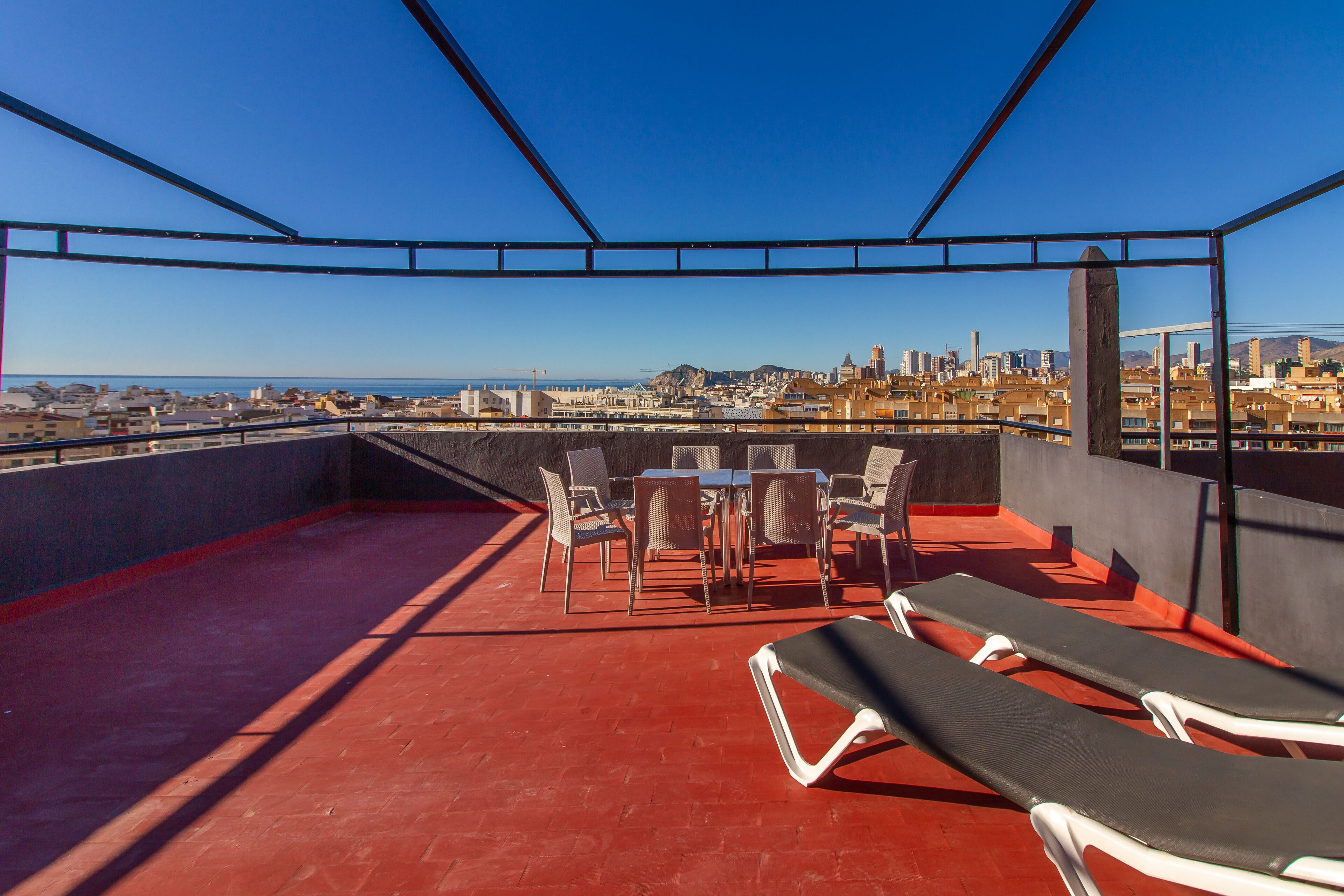 Una terraza en la azotea con mesa y sillas, sillones de descanso y vistas a la ciudad.