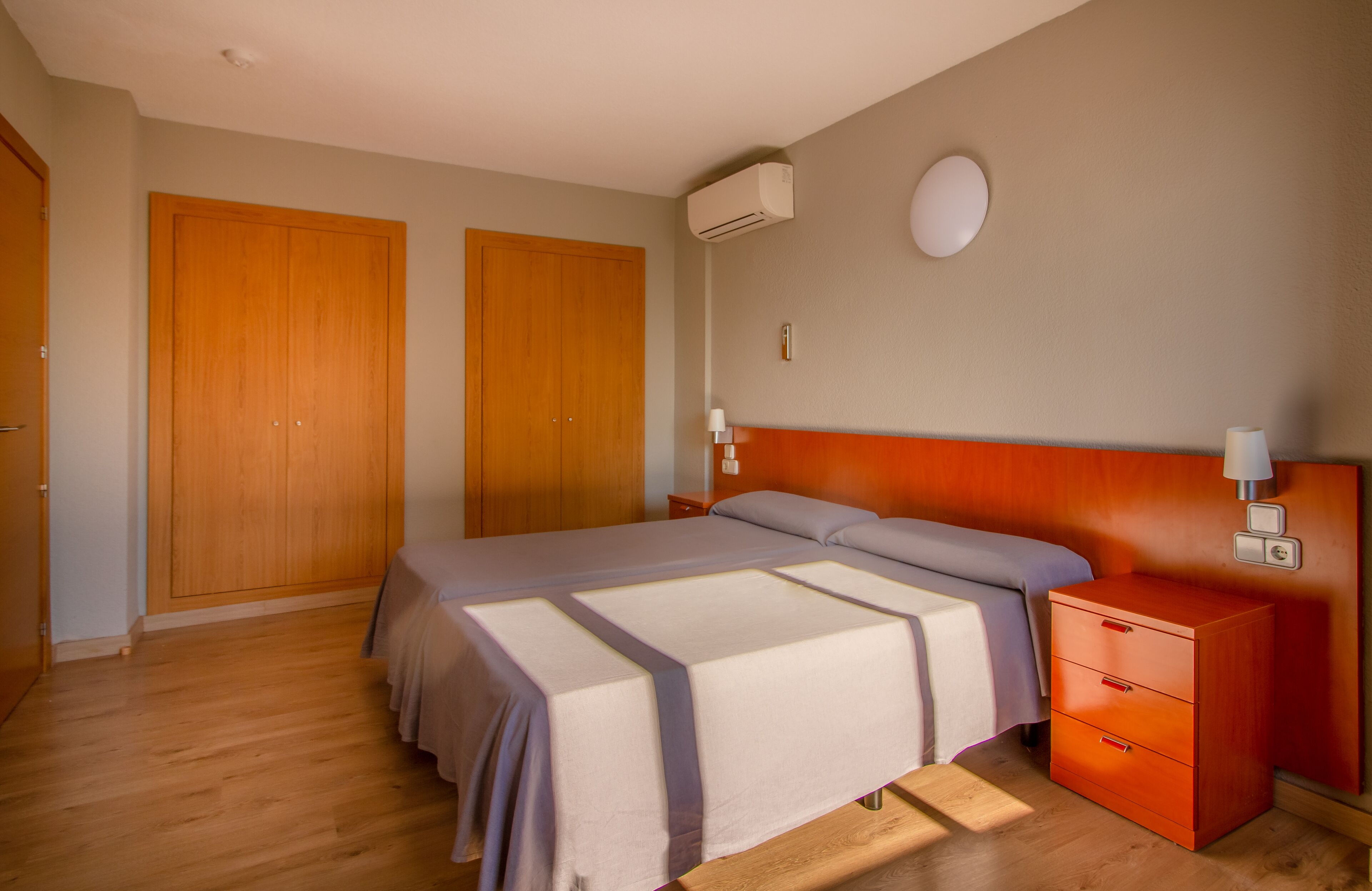 A bedroom with a bed, wooden wardrobe, nightstand, and an air conditioning unit.