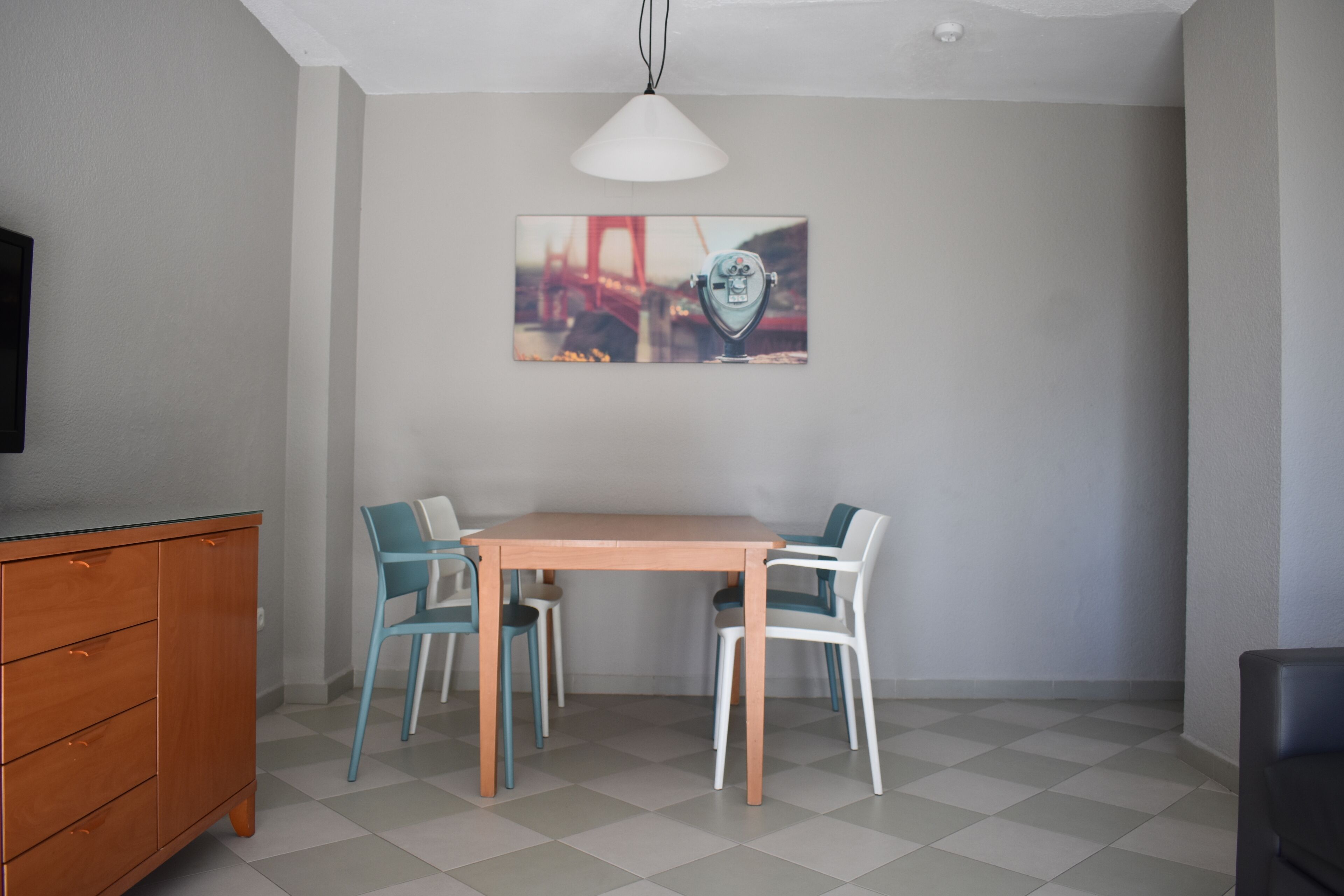 A dining area with a wooden table and chairs, a painting on the wall, and a television on the left.