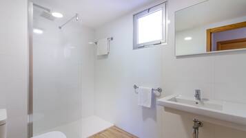 Un baño moderno con cabina de ducha de vidrio, inodoro, lavabo y espejo.