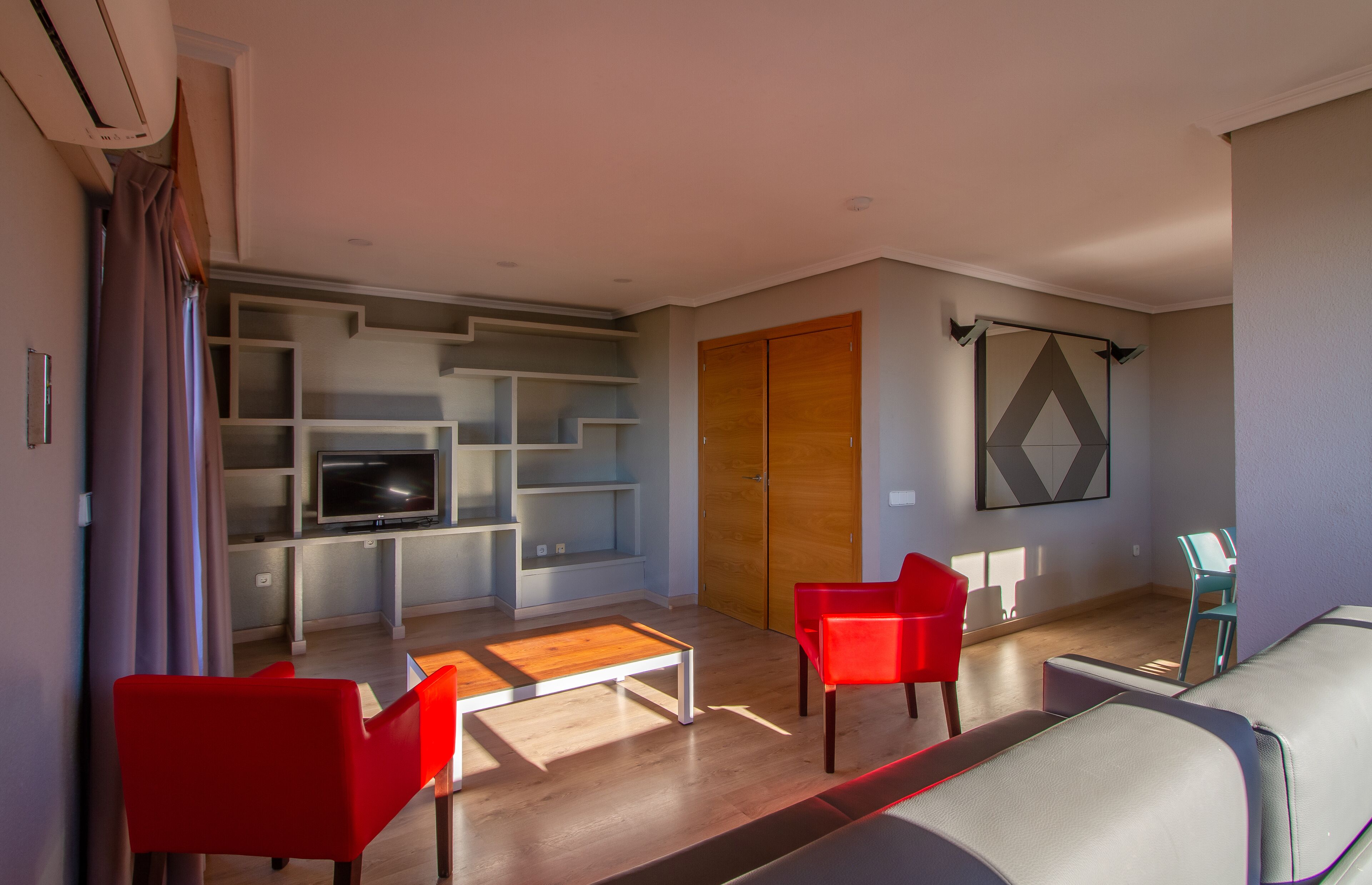 Un salon moderne avec un téléviseur à écran plat, des fauteuils rouges, une table basse en bois et un canapé.