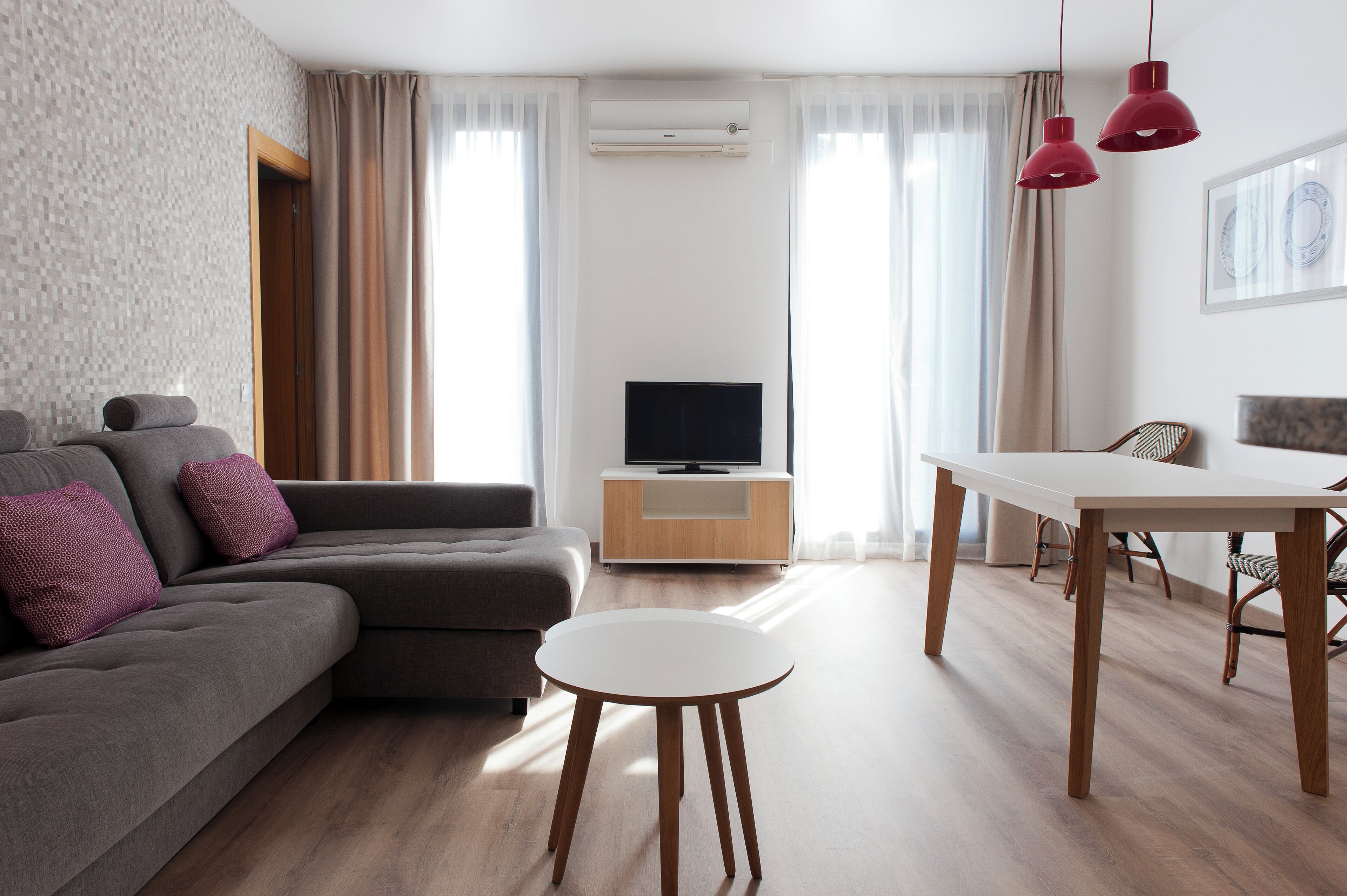 A modern living room with a sofa, a round table, and a television on a wooden cabinet.