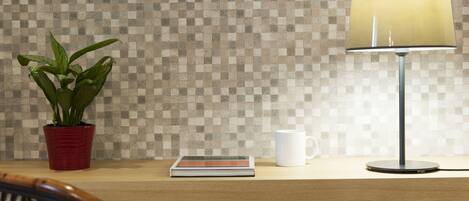 A wooden desk with a checkered tile wall, a potted plant, a lamp, a book, and a white mug.