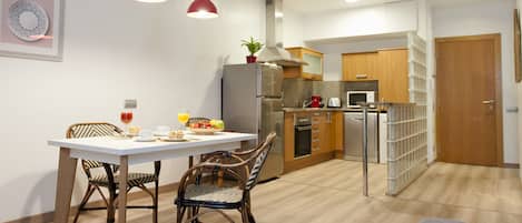 A modern kitchen with a dining area, featuring a white table, wicker chairs, and a red pendant light.