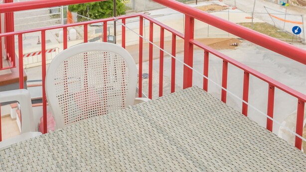 A balcony with a view of the sea, a red railing, and a white chair.