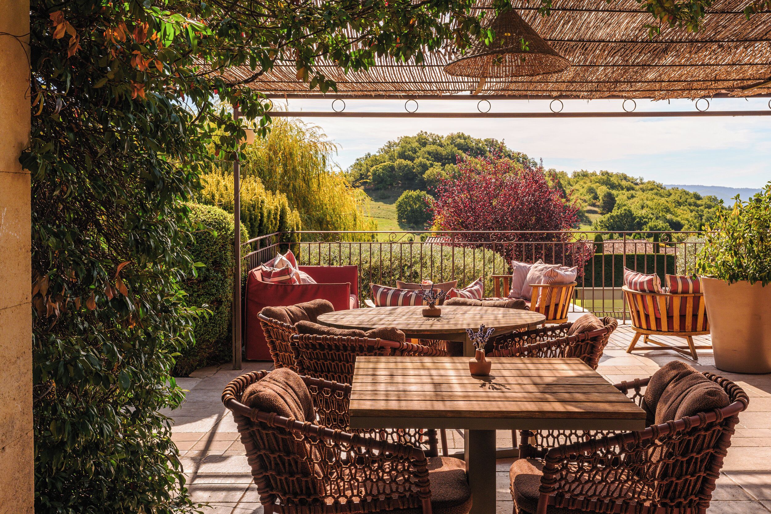 An outdoor patio with wicker furniture, a round table, and a view of a lush landscape.