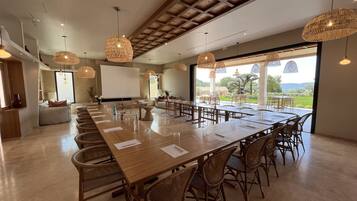 A spacious conference room with a long wooden table, wicker chairs, and large woven pendant lights.