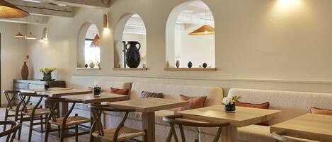 A cozy restaurant interior with wooden tables and chairs, arched windows, and hanging pendant lights.