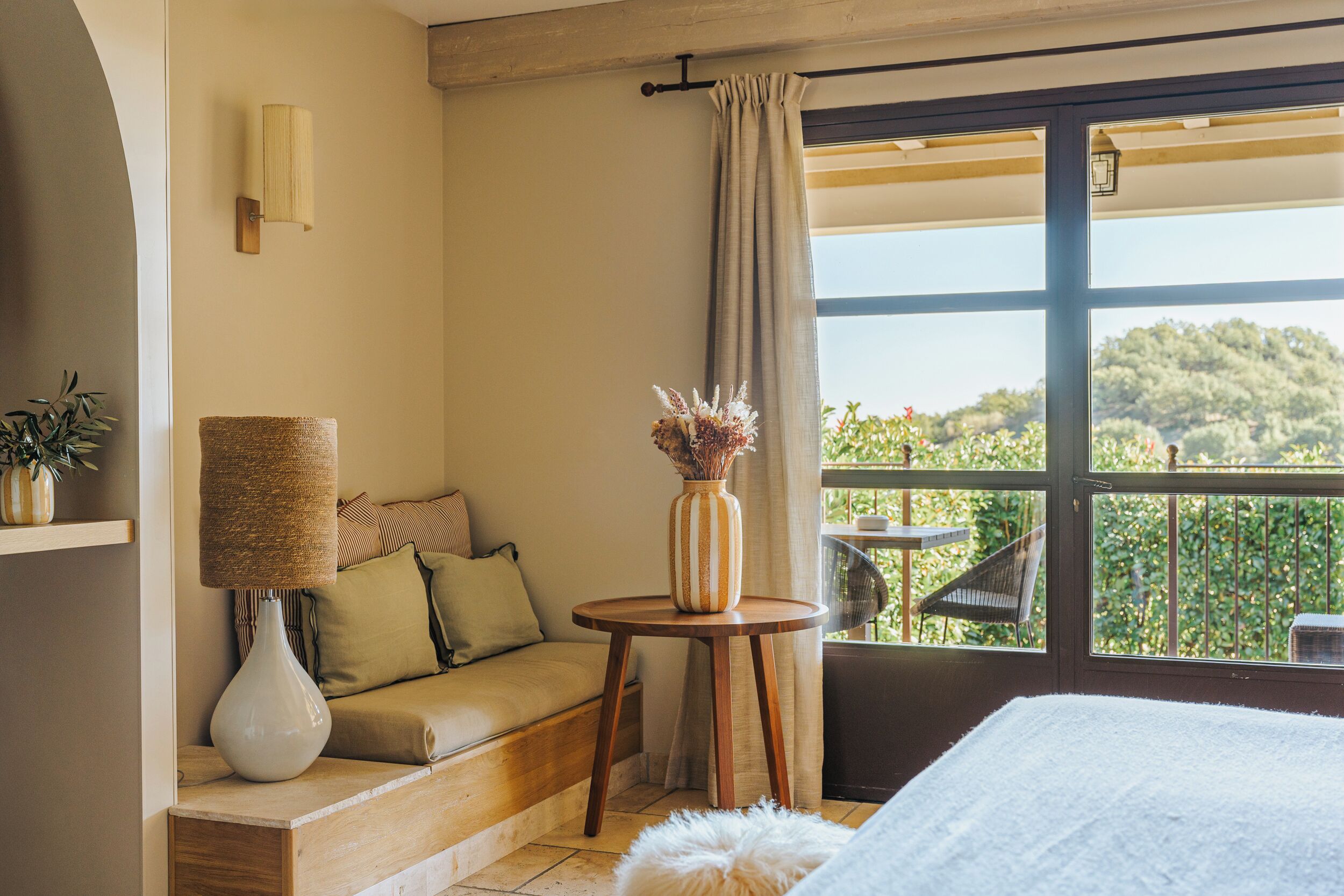 Una habitación con sofá, una mesita con un florero, una lámpara y vistas a zonas verdes a través de amplias ventanas.