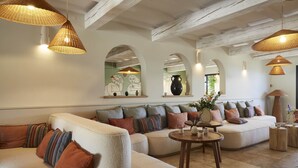 A spacious living area with a large beige sofa, multiple cushions, and a round wooden coffee table. There are wicker pendant lights and a large vase on a side table. - La Bastide Saint Georges (Forcalquier)
