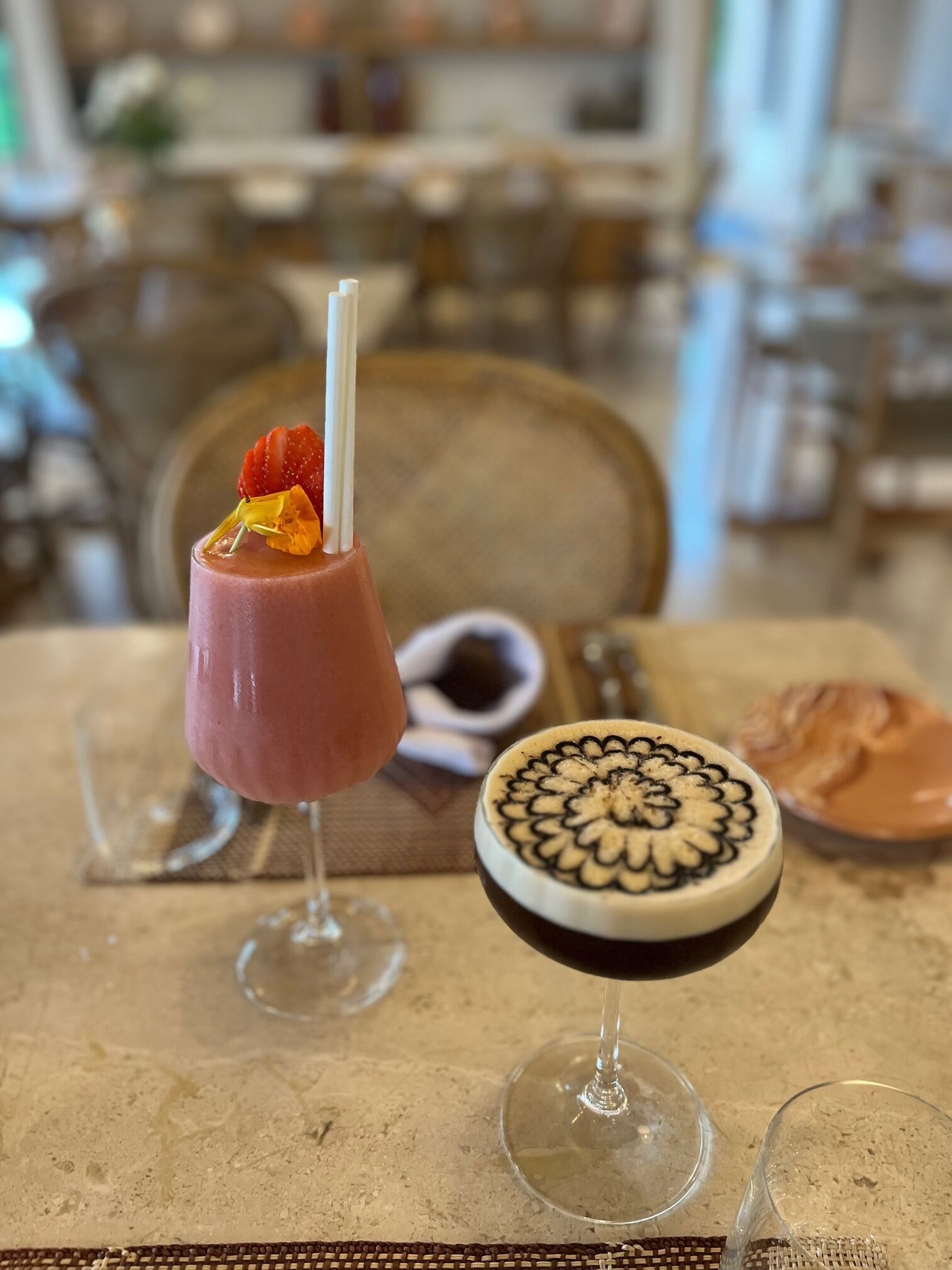 Una mesa con dos bebidas, una en un vaso y otra en un tazón, y un plato pequeño de comida.
