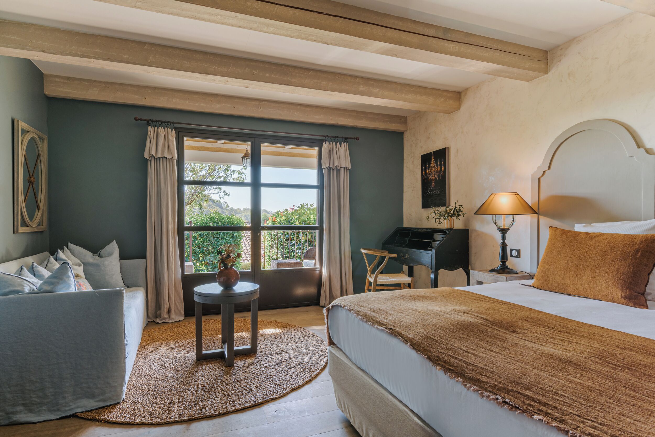 A bedroom with a bed, a desk, a chair, a sofa, and a view of the outdoors.