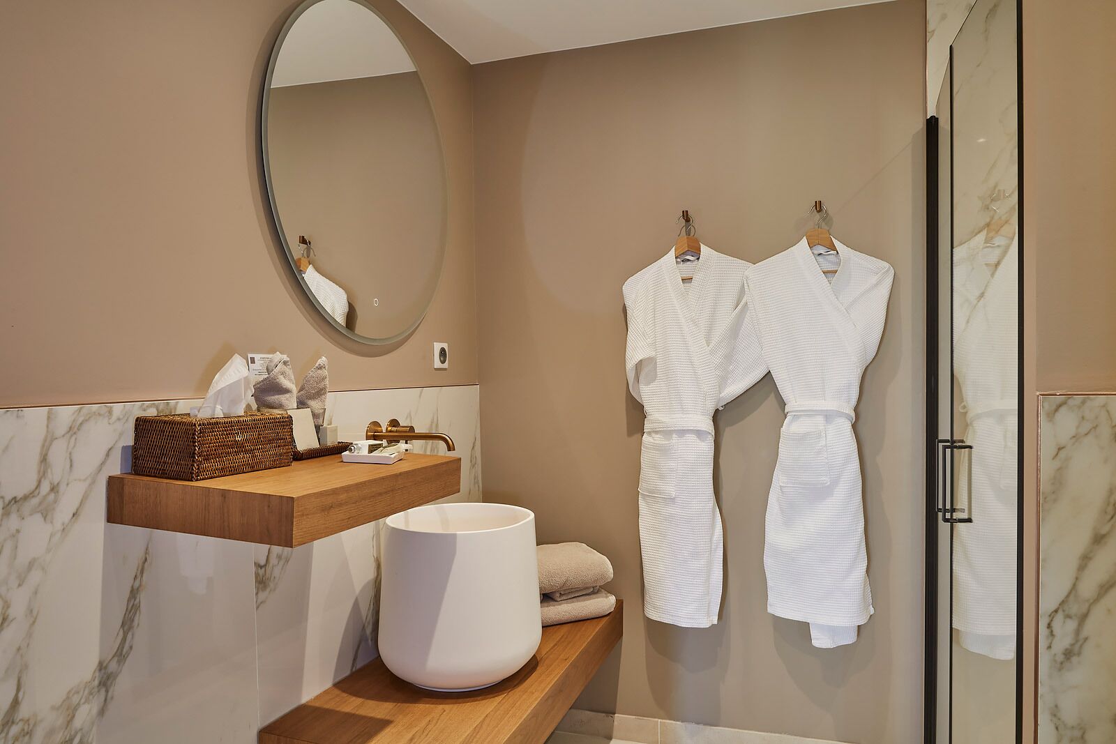 Un baño moderno con tocador de mármol, un espejo grande y dos albornoces blancos colgados en ganchos.