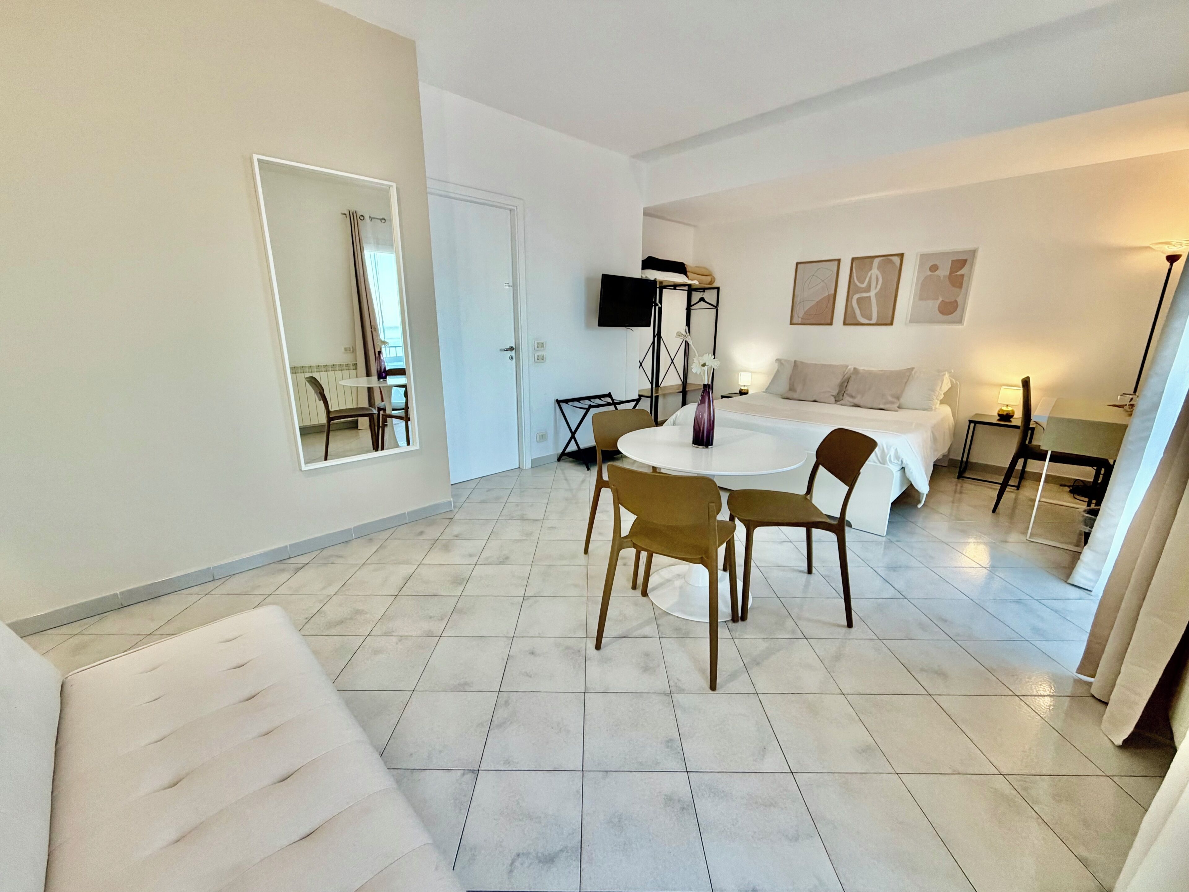 Habitació d'hotel moderna amb un llit, una taula rodona de dinar amb cadires, una televisió i obres d'art a les parets.