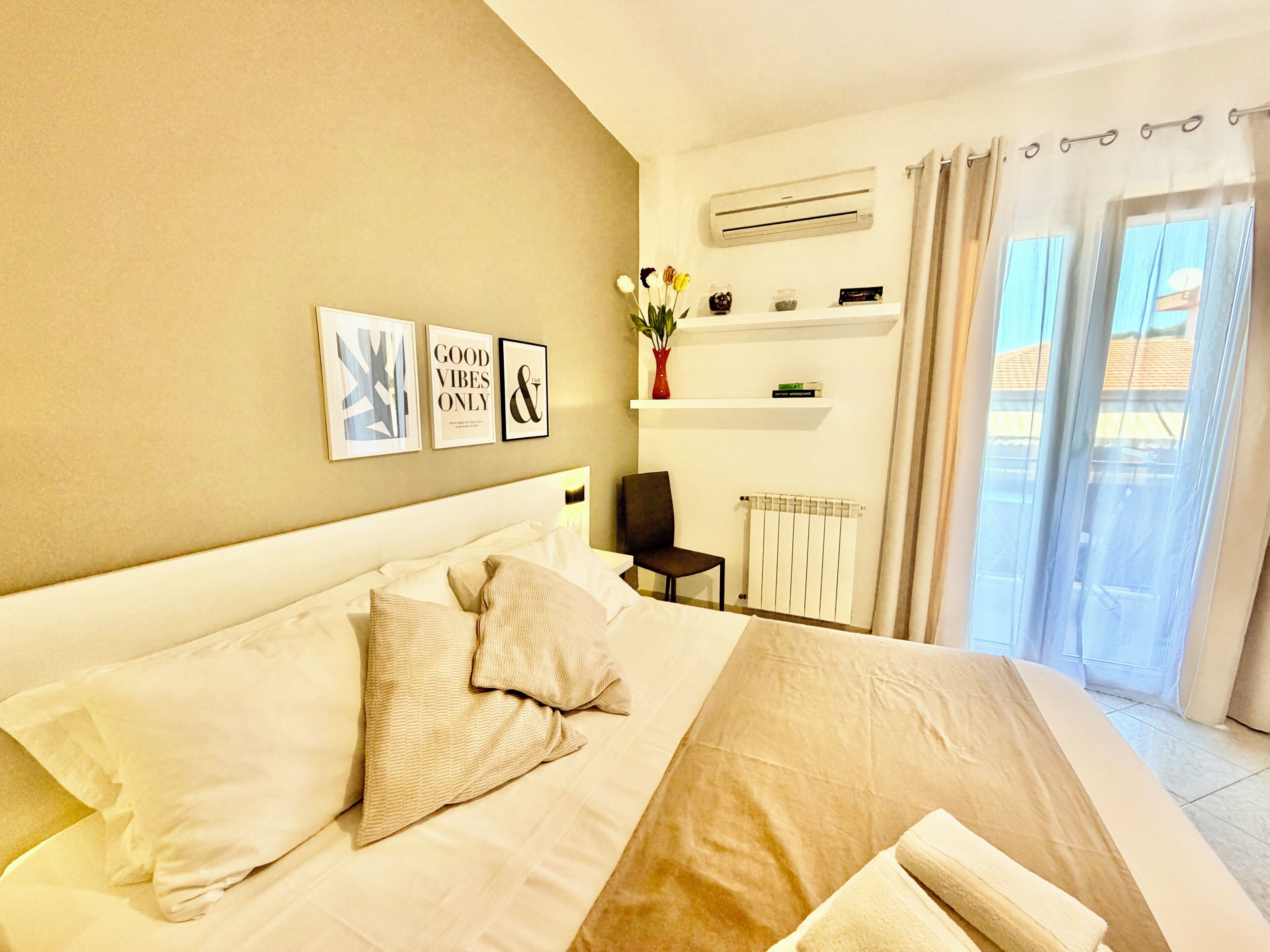 Une chambre d’hôtel avec un lit, une chaise, un radiateur, une étagère avec des livres et une fenêtre avec des rideaux.