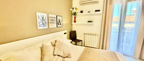 Une chambre d’hôtel avec un lit, une chaise, un radiateur, une étagère avec des livres et une fenêtre avec des rideaux.