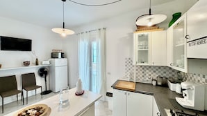 A modern kitchen with a central island, white cabinetry, a microwave, a refrigerator, and a gas stove. - Ma&Mi Guest House (Cefalù)